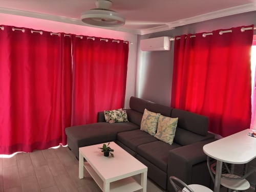 Moderna sala de estar en ALOE Lovers Suite con sofá oscuro, mesa de centro rosa y cortinas rojo vibrante en Apartamentos Aloe,