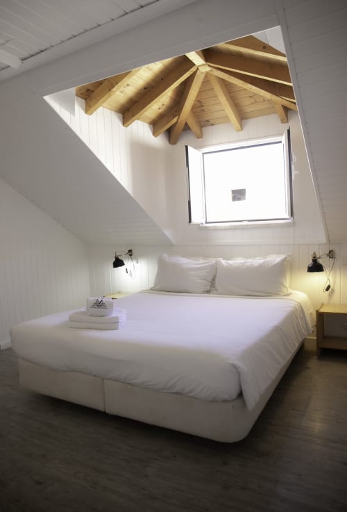 Quarto moderno em sótão da Vinnus Guesthouse em Ericeira com claraboia, vigas de madeira e roupa de cama branca