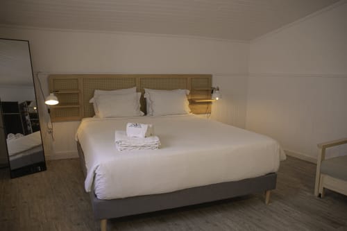 Quarto luminoso na Pousada Vinnus Ericeira com cama de casal, cabeceira em rattan, piso de madeira e vista para a cidade