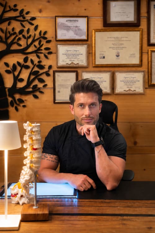 Osteopata professionista presso il Ristorante Hotel Moderno a Serina BG, Italia, con modello della colonna vertebrale e diplomi esposti dietro la scrivania