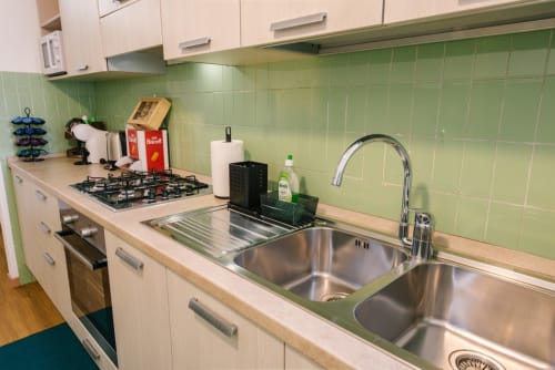 Moderna cucina nell'appartamento di Verona con lavello doppio in acciaio inox, piano cottura a gas, piastrelle verdi e mobili bianchi.