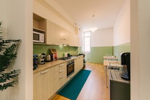 Cucina moderna nell'appartamento di Verona con pensili in legno chiaro, rivestimento verde, elettrodomestici in acciaio e tappeto turchese