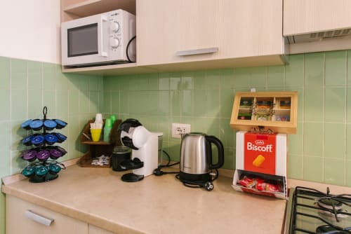 Piano cucina dell'appartamento di Verona con macchina da caffè, bollitore, microonde e contenitore di tè vicino alla parete di piastrelle verdi