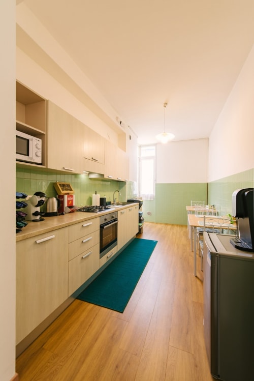 Cucina moderna con mobili in legno chiaro, rivestimento in piastrelle verdi e pavimenti in legno nell'appartamento di Verona