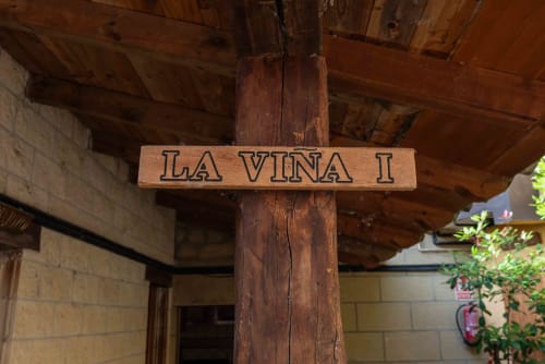 Wooden sign reading 'LA VIÑA I' hanging from rustic beam at Casas Rurales La Viña in Cuzcurrita de Río Tirón