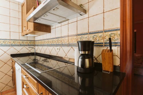 Modern kitchen at Casas Rurales La Viña with black countertop, electric cooktop, wooden cabinets, and decorative tile