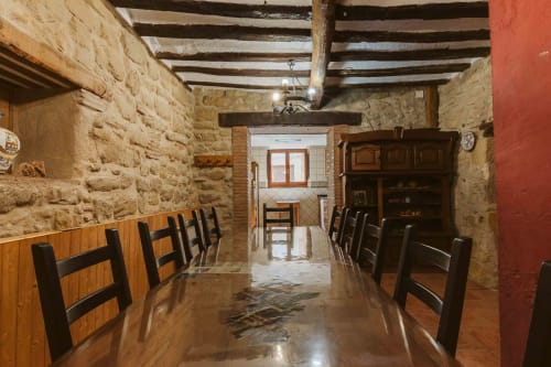 Rustic dining room in La Viña 1 apartment at Casas Rurales with stone walls, wooden beams, and long table with chairs
