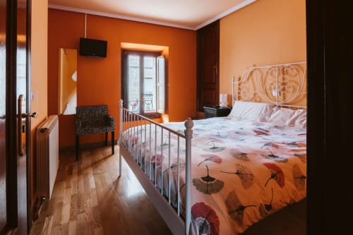 Bright orange bedroom at Casas Rurales La Viña with metal bed frame and patterned bedding overlooking balcony