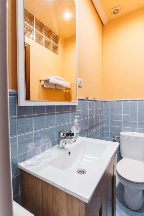 Modern bathroom in La Viña apartment at Casas Rurales with white sink, toilet, yellow walls, blue tile backsplash, and mirror