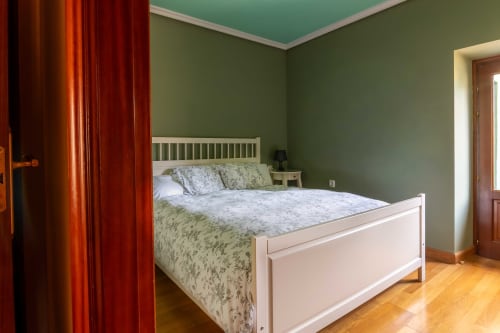 Bright bedroom at Casas Rurales La Viña with white bed, sage green walls, turquoise ceiling, and hardwood floors