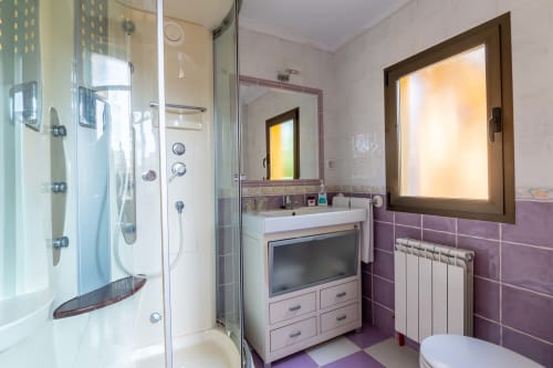 Modern bathroom at Casas Rurales La Viña with purple tiled walls, glass shower enclosure, vanity with storage, heated towel