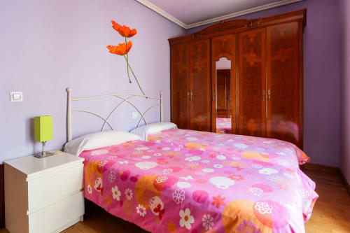 Bright bedroom at Casas Rurales La Viña with purple walls, floral bedding, wooden wardrobe, and orange flowers on nightstand