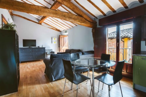 La Viña 2 apartment living space with wooden beams, dining table, sofa, TV, and balcony overlooking Cuzcurrita de Río Tirón