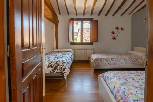 Bedroom at Casas Rurales La Viña with three beds, wooden beams, window, and floral decorations in Cuzcurrita de Río Tirón