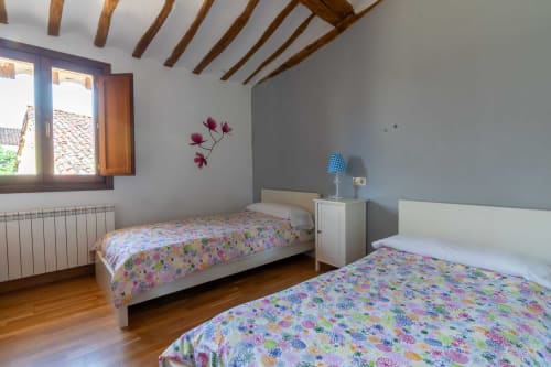 Bright bedroom with two single beds, exposed wooden beams, and colorful floral bedding at Casas Rurales La Viña rural