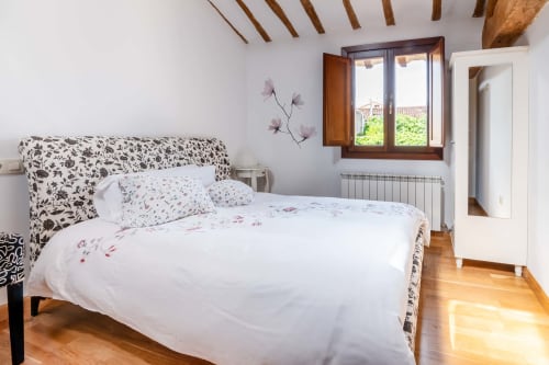 Bright bedroom at La Viña 2 rural apartment in Cuzcurrita de Río Tirón with floral bedding, wooden beams, and garden views
