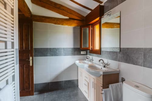 Modern bathroom in La Viña 2 apartment at Casas Rurales with dual sinks, tiled walls, wooden beams, and heated towel rack