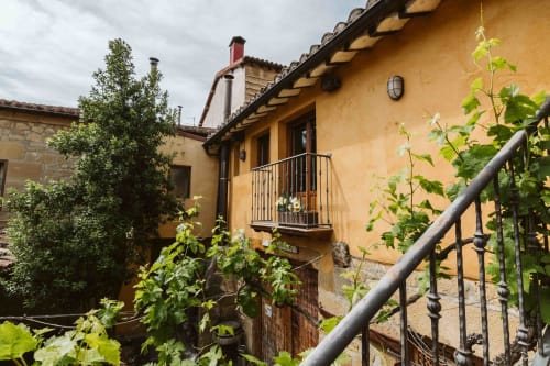 Rustic yellow stone apartment at Casas Rurales La Viña with balcony, climbing vines, and charming courtyard entrance in