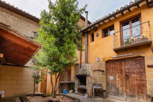 Rustic stone courtyard at Casas Rurales La Viña in Cuzcurrita de Río Tirón with yellow building, wooden doors, and