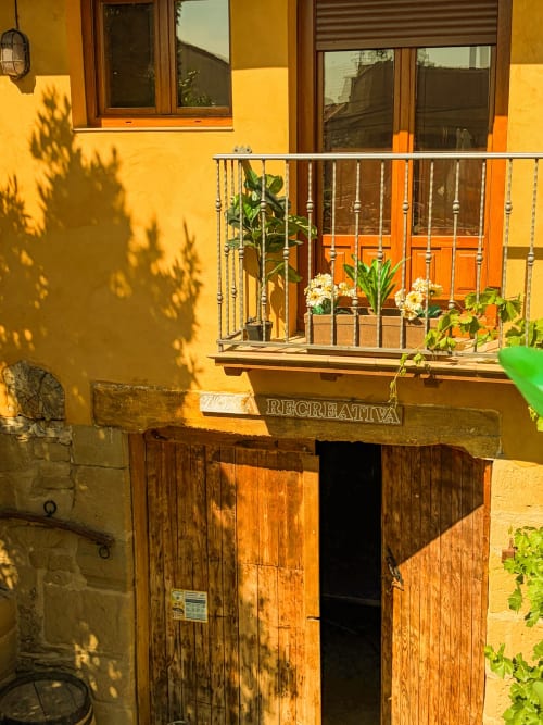 Sunny balcony with white railing, potted flowers, and orange doors at Casas Rurales La Viña in Cuzcurrita de Río Tirón, Spain