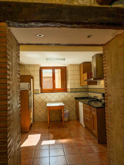 Spacious kitchen at Casas Rurales La Viña with wooden cabinets, tiled walls, terracotta floor, and access to outdoor patio