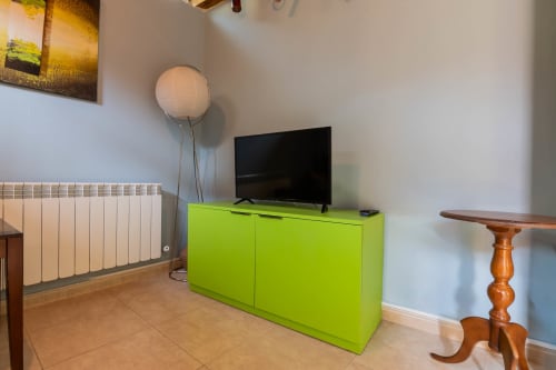 Bright living room at Casas Rurales La Viña with lime-green TV cabinet, flat-screen TV, white radiator, and wooden furniture