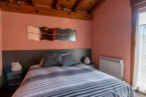 Cozy bedroom at Casas Rurales La Viña with coral walls, striped bedding, wooden beams, and modern radiator heating.