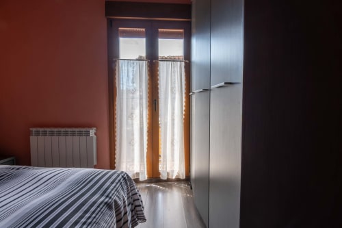 Cozy bedroom at Casas Rurales La Viña with striped bed, radiator, balcony doors with white curtains, and modern refrigerator