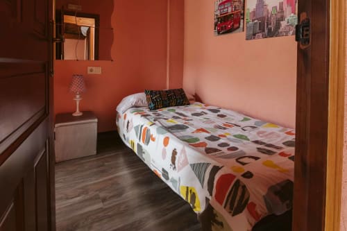 Cozy bedroom at Casas Rurales La Viña with coral walls, colorful bedding, and rustic wooden flooring