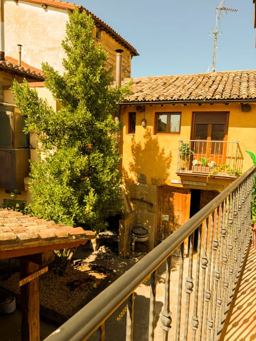 Sunny courtyard of Casas Rurales La Viña with yellow buildings, terracotta roof, climbing ivy, and metal railing in