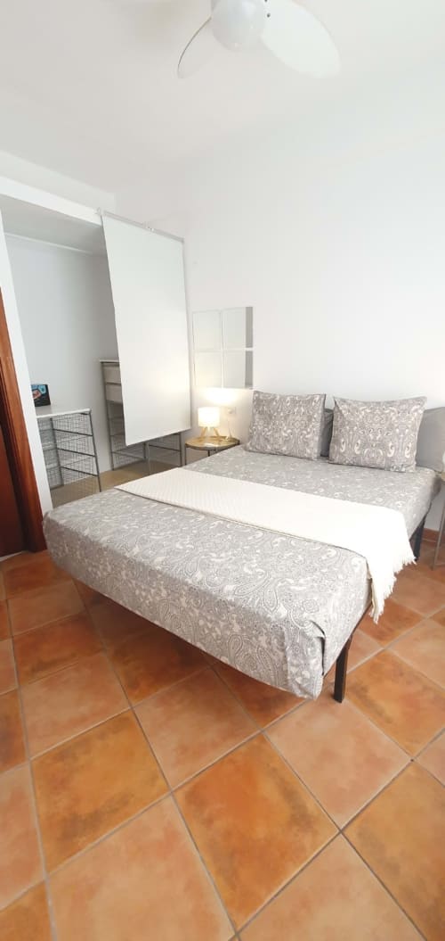 Dormitorio en Casa Juana de El Médano con ropa de cama estampada, lámpara y piso de baldosas de terracota
