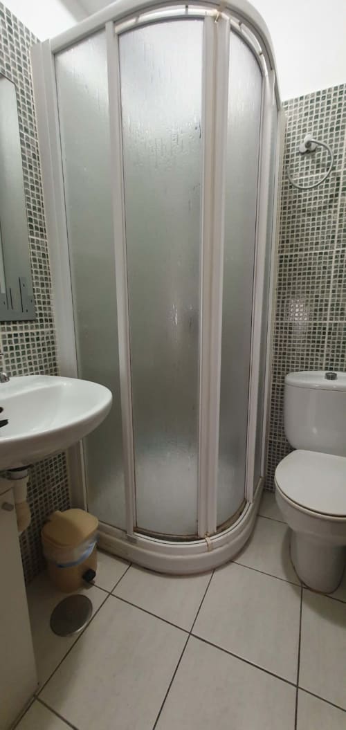 Baño compacto en apartamento Casa Juana, El Médano, con ducha de cristal curvo, lavabo blanco e inodoro