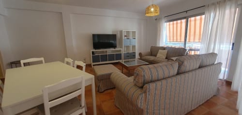 Luminoso salón en El Médano con sofá a rayas, mesa de comedor blanca, TV, mueble de almacenaje y acceso a balcón