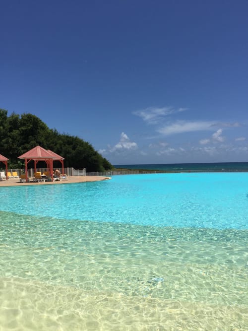 Piscine lagon turquoise à l'Appartement Kfé Chocolat avec gazebo rouge, chaises longues et vue sur l'océan en Guadeloupe