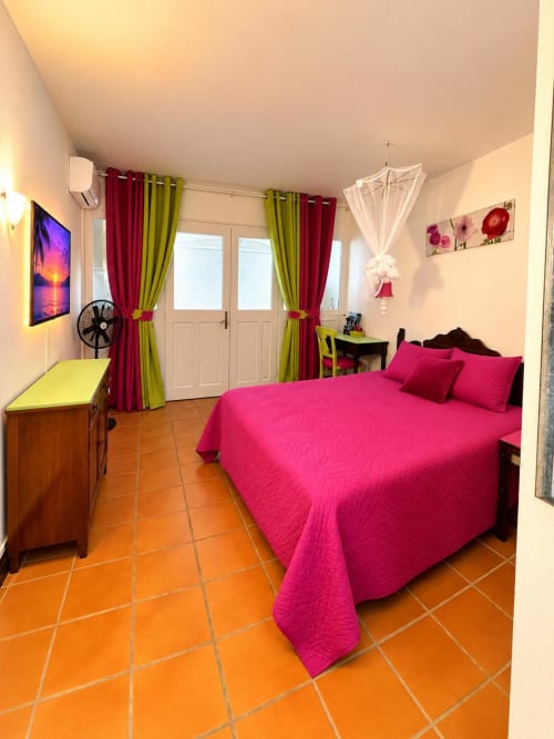 Chambre vibrante au Kfé Chocolat avec literie rose, rideaux colorés, carrelage en terre cuite et accès au balcon