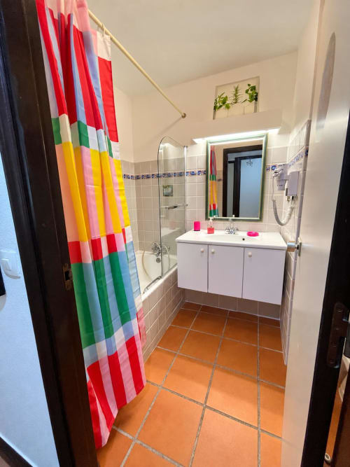 Salle de bain lumineuse à l'Appartement Kfé Chocolat avec rideau de douche rayé coloré, meuble blanc, carrelage orange et verre