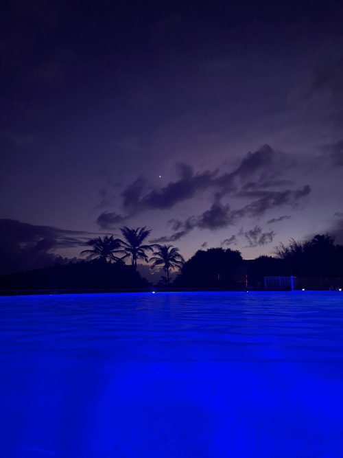 Piscine illuminée au crépuscule avec palmiers en silhouette sur le ciel du soir à l'Appartement Kfé Chocolat