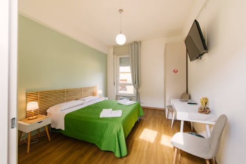 Camera luminosa al 3 Guest House Verona con coperta verde, pavimento in legno, scrivania, TV e arredi moderni
