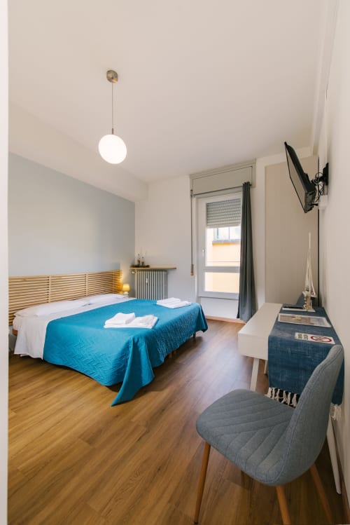 Camera moderna presso 3 Guest House Verona con letto in legno, coperta blu, pavimenti in legno e arredi contemporanei