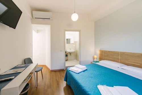 Camera moderna alla 3 Guest House Verona con coperta blu, testata in legno, scrivania e bagno privato