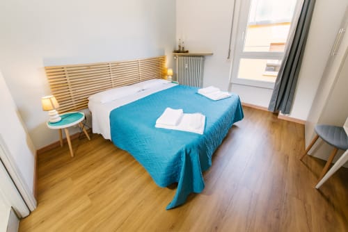 Camera da letto moderna a Verona con letto blu, pavimento in legno, testiera lignea e accesso al balcone