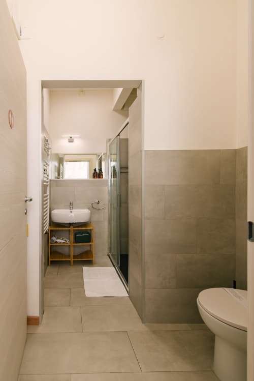 Moderno bagno dell'appartamento di Verona con doccia aperta, lavabo a bacinella, toilette e mobile in legno con specchio