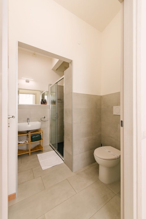 Bagno moderno nell'appartamento di Verona con toilette, doccia aperta, lavabo e rivestimento in piastrelle beige