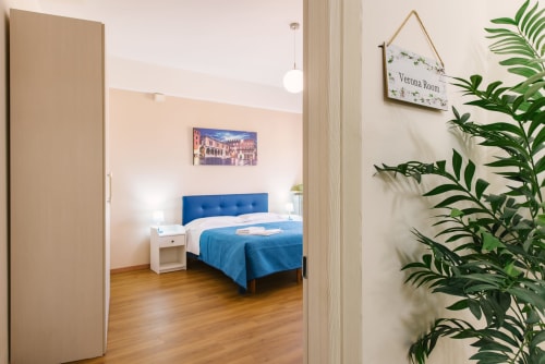 Camera da letto dell'appartamento di Verona con letto blu, comodino bianco e pavimento in legno vicino all'ingresso ospiti