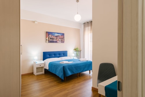 Camera da letto moderna in appartamento veronese con letto imbottito blu, comodino bianco e pavimentazione in legno