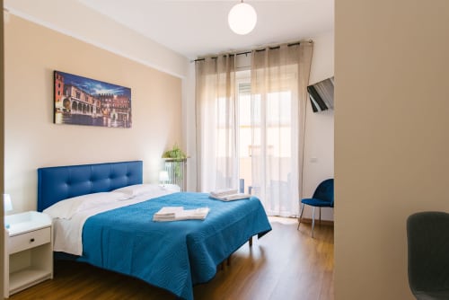 Camera luminosa in appartamento veronese con letto imbottito blu, comodino bianco, accesso al balcone e arredi moderni