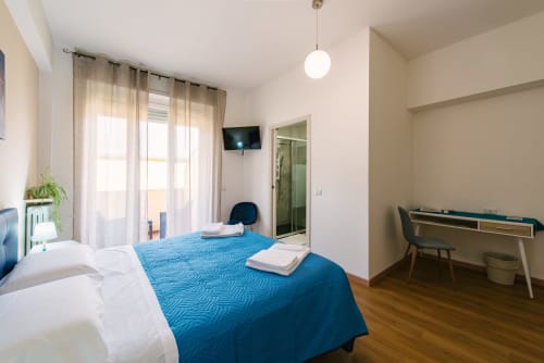 Luminosa camera da letto a Verona con letti gemelli, biancheria blu, scrivania, TV e accesso al balcone con vista sulla città.