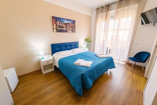 Camera da letto moderna a Verona con letto rivestito in blu, comodino bianco, pavimenti in legno, accesso al balcone