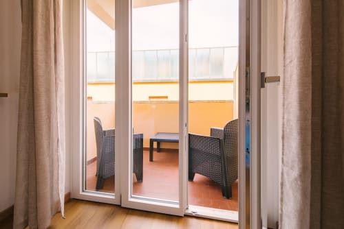 Accesso moderno al balcone dell'appartamento di Verona con porte in vetro, sedie in vimini e terrazza con vista sulla città