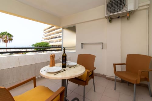 Modern studio apartment balcony in Costa Adeje with dining table, chairs, and sea view over pool area